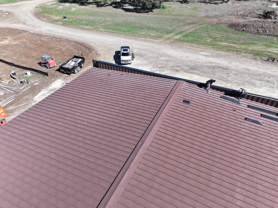 Aerial view of an industrial building in Texas with a new brown standing seam metal roofing system under construction.